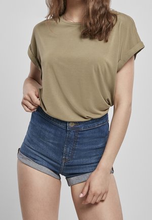 Frau trägt ein olivgrünes T-Shirt mit hochgekrempelten Ärmeln und blaue Denim-Shorts mit hochgekrempeltem Saum und Knopfverschluss, auf die Mitte des Oberschenkels gekürzt.
