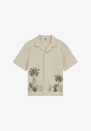 Chemise beige à manches courtes boutonnée avec impressions vertes de palmiers tropicaux et de feuilles sur le bas devant.