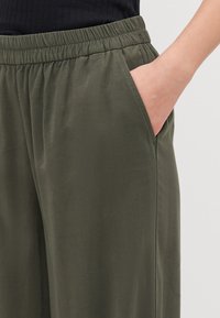 Olive green trousers with an elastic waistband, featuring side pockets and a smooth, lightweight fabric texture.