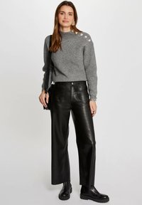 Pull gris à côtes avec des boutons décoratifs à l'épaule, associé à un pantalon large en cuir noir taille haute et des bottines noires.
