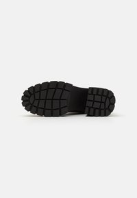 Suela de zapato de goma negra con patrones profundos y estriados para un mejor agarre. Forma plana y ancha, con material flexible y bordes reforzados.