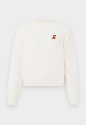 Bijeli pleteni pulover s rebrastom teksturom, s malim vezom smešnog medvedića na prsima. Okrugli izrez i duge rukave.