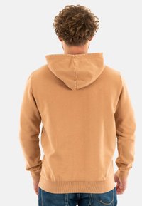 Sudadera con capucha en tejido beige con un acabado texturizado, que presenta puños y dobladillo en canalé. La parte trasera es lisa con un detalle de costura central.