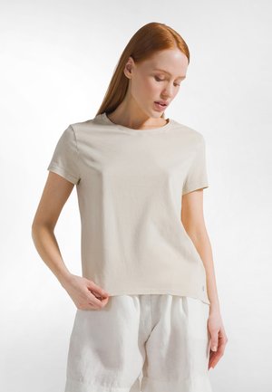 Beige katoenen T-shirt met korte mouwen, ronde hals en een losse pasvorm, gecombineerd met witte linnen broek, voorzien van subtiele stiksel details.