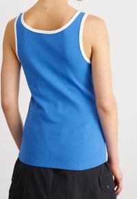 Ribbad blå ärmklänning med vit kant, med en åtsittande design och rund halsringning. Synlig textur på tyget, bakvy visas.