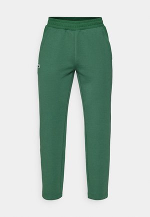Pantaloni della tuta verde scuro con vita elastica, tasche laterali e un piccolo logo. Texture liscia e design con gamba affusolata.