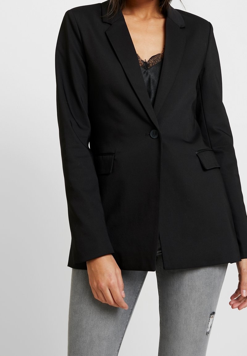 Blazer nero con chiusura a un bottone, rever a punta e due tasche frontali. Tessuto liscio, design sartoriale e vestibilità leggermente strutturata.