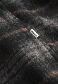 Grå og sort ternet uldstof med blød tekstur, der har et GABBA brandingmærke. Subtile brune accenter i mønsteret.