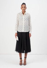 Sheer white blouse with black polka dots, paired with a black tulle midi skirt. Accessories include a small white clutch and black strappy heels.