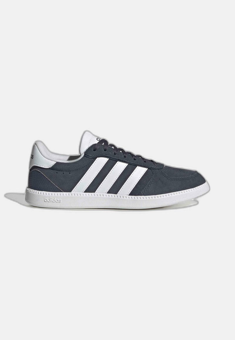 Zapatillas de ante gris oscuro con detalles en blanco. Presenta tres rayas blancas, cordones redondos y una suela de goma blanca. Diseño clásico.