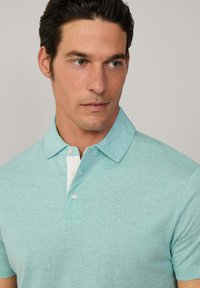 Polo de color azul claro con cuello, dos botones y una tapeta blanca. El material parece suave con una textura sutil.