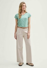 Top de manga corta en verde menta con lunares blancos, combinado con pantalones anchos beige, un cinturón marrón y sandalias marrones con suela texturizada.