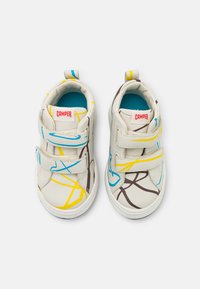 Des chaussures en cuir blanches avec des motifs abstraits bleus, jaunes et marron. Dotées de deux brides Velcro et d'une doublure intérieure turquoise.