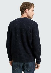 Dunkelblauer Strickpullover mit strukturiertem Design, ausgestattet mit mehrfarbigen/Flecken, Rundhalsausschnitt und gerippten Bündchen, kombiniert mit Jeans.