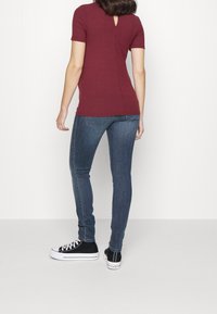 Top corto de manga corta a rayas color burdeos con detalle de abertura en la espalda, combinado con jeans ajustados de lavado oscuro y zapatillas negras de corte bajo.