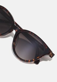 Óculos de sol em padrão tartaruga com design oversized de olhos de gato, lentes em gradiente escuro e detalhes em tom dourado nas hastes. Armação em plástico texturizado.