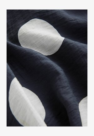 Marinblått tyg med stora vita cirklar. Materialet verkar lätt och har en mjuk textur, med en slät, något rynkad yta.