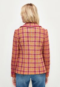 Blazer en tweed avec un motif à carreaux multicolores en orange, rose et noir. Dispose d'un col cranté et d'une silhouette cintrée.