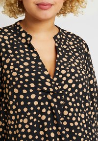 Blusa in tessuto nero con scollatura a V e motivo maculato beige, dal taglio rilassato e dalla texture morbida. Maniche corte leggermente arrotolate.