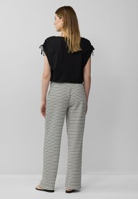 Zwarte short-sleeve top met strikdetails op de schouders, gecombineerd met hooggekamde, wijde pantalons met een zwart-wit gestreept patroon.