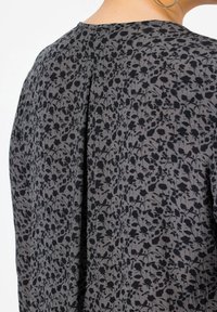 Un tissu gris texturé présente un motif floral noir. Le design inclut un léger plissage à l'arrière, rehaussant l'apparence générale.