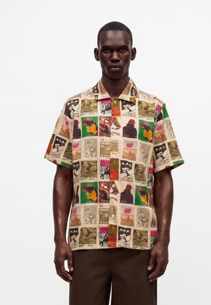 Homme portant une chemise à manches courtes boutonnée avec un imprimé coloré de style collage composé de diverses images artistiques et de textes.