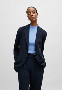 Marinblå skräddarsydd blazer med slag, tillsammans med en ljusblå ribbad tröja och matchande högmidjade byxor med ett silverfärgat spänne.