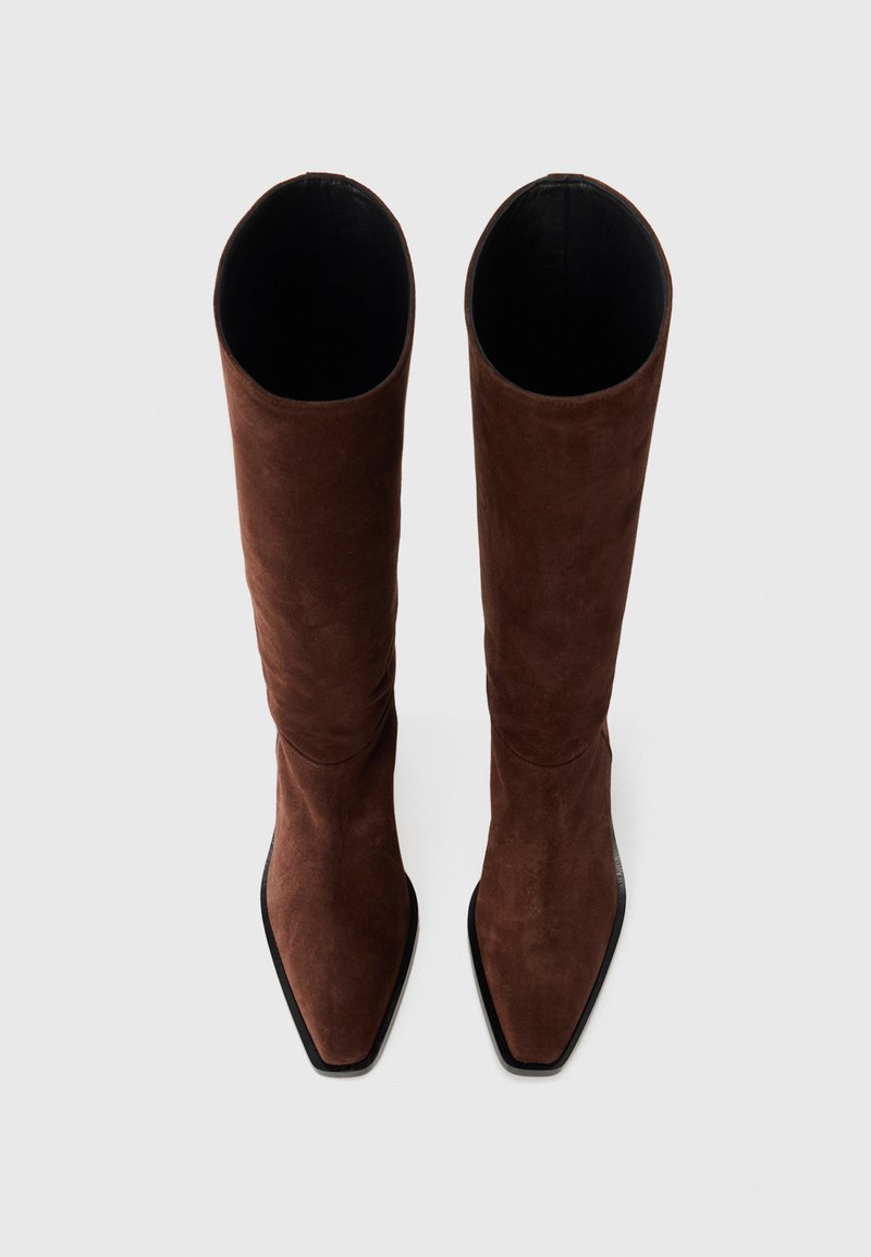 Brown suede knee-high boots with a pointed toe and flat black sole, featuring a smooth texture and cylindrical shape.