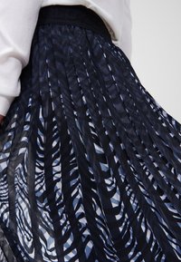 Jupe plissée avec un motif abstrait bleu marine et bleu clair. Fabriquée en matériau léger, elle dispose d'une taille élastique noire.