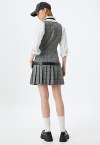 Vestido a cuadros gris con falda plisada, banda negra en la cintura, mangas de camisa blancas y una gorra oscura. Unas zapatillas gruesas negras completan el look.