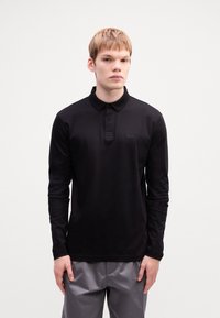 Black long-sleeve polo shirt made of smooth fabric, featuring a buttoned collar and subtle logo detail on the chest.