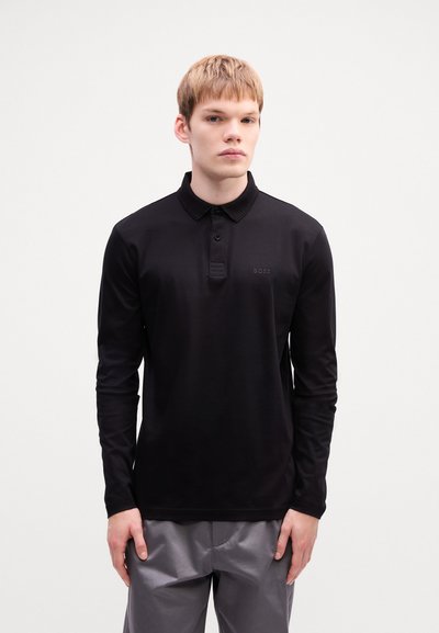 Polo noir à manches longues en tissu lisse, doté d'un col à boutons et d'un logo discret sur la poitrine.