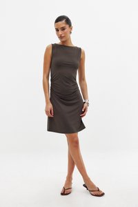 Ärmelloses, braunes Kleid mit gerafften Details an der Seite. Glatter, dehnbarer Stoff; knielanger Saum, flache Sandalen, minimale Accessoires.