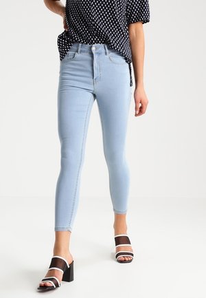 Osoba nosząca jasnoniebieskie obcisłe dżinsy, czarno-biały top w groszki oraz czarne sandały na słupku z białymi paskami.