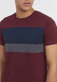 Kortærmet crewneck T-shirt i bordeaux med horisontale striber i marineblå og grå. Materialet er en bomuldsblanding med en glat tekstur.
