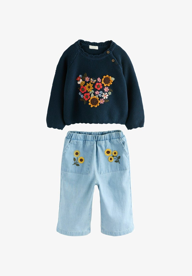 Marineblauer Strickpullover mit bunter Blumen- und Bienenstickerei, kombiniert mit hellblauen Hosen mit gelber Blumenstickerei auf den Taschen.