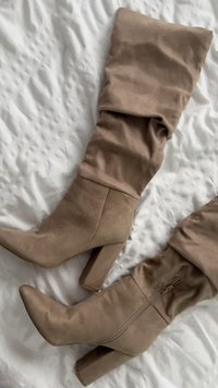 Par visokih čizama od taupe antilopa s debelim potpeticama i bočnim patentnim zatvaračima, položenih ravno na bijelu tkaninu s teksturom.