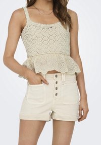 Top de punto color beige claro con dobladillo festoneado y tirantes anchos, combinado con pantalones cortos de talle alto en beige claro que cuentan con cinco botones en la parte delantera.