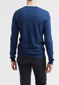 Marinblå tröja, rund hals, långa ärmar, ribbade muddar och fåll, tillverkad av mjukt stickat material. Minimalistisk design, utan ytterligare mönster eller detaljer.