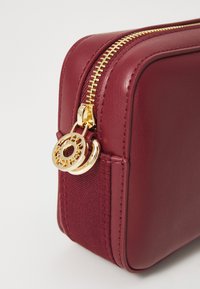 Burgunderfarbene Lederkosmetiktasche mit goldfarbenem Reißverschluss und kreisförmigem Hardware-Detail. Texturierte Seitenwand erhöht das visuelle Interesse. Kompakte rechteckige Form.