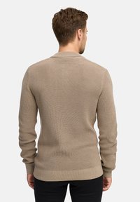 Maglione a coste beige con maniche lunghe, collo rotondo e vita aderente. La texture è lavorata, offrendo un motivo sottile.