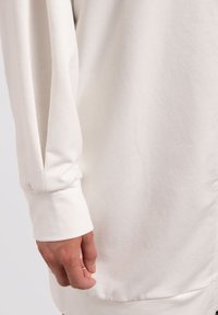 Camicia a maniche lunghe in cotone bianco, caratterizzata da una vestibilità rilassata e una texture morbida. I polsini sono svasati, con una cucitura visibile all'orlo.