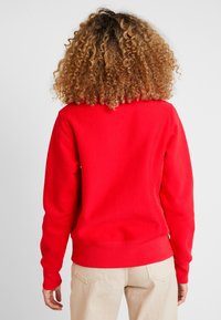 Rode sweatshirt met een ronde halslijn, ribgebreide manchetten en zoom. Gladde textuur en ontspannen pasvorm, met stikdetails op de rug.