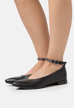 Ballerines noires en cuir avec un petit talon, présentant un bout pointu et une bride de cheville ornée de perles décoratives.