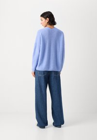 Lichtblauwe gebreide trui met een relaxed fit, ronde hals en verlaagde schouders, gecombineerd met loszittende blauwe jeans.