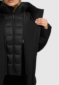 Zwarte pufferjack met een hoge kraag en een rits aan de voorkant, met een gewatteerd ontwerp en een gladde textuur. Geopend om de binnenvoering te tonen.
