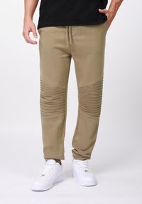 Μπεζ παντελόνι jogging με ραβδώσεις στα γόνατα, κατασκευασμένο από μαλακό ύφασμα. Διαθέτει ελαστική μέση με κορδόνι και πλαϊνές τσέπες.