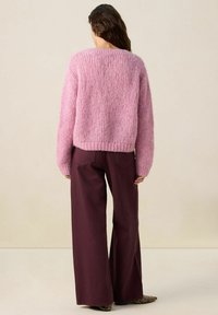 Pull en maille rose avec un tissu texturé, coupe décontractée et ourlet à côtes. Associé à un pantalon ample bordeaux foncé.