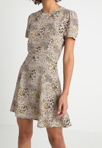 Robe à manches courtes à imprimé floral beige, avec un corsage ajusté, une jupe évasée, un tissu texturé et des accents subtils noirs et jaunes.