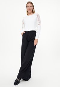 Blusa blanca de manga larga con bordado floral en las mangas, combinada con pantalones de pierna ancha de talle alto negros y mocasines negros.